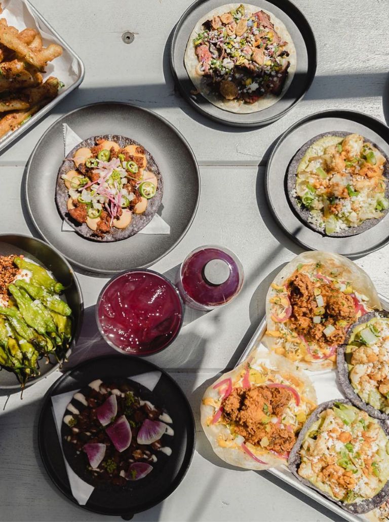 A table at Tacoparty covered brightly colored tacos, shishito peppers, radishes and a bright purple drink.